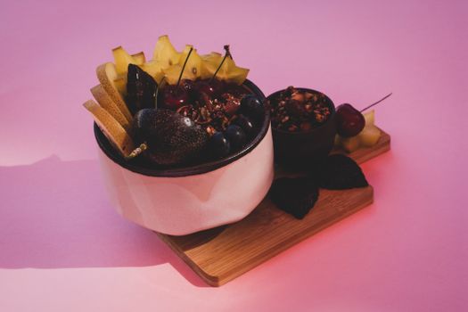 Colorful display of mixed fruit and granola in bowls on a pink background, perfect for healthy eating concepts.