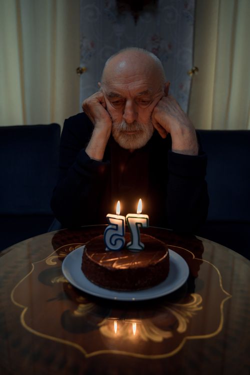 Free Elderly man sits alone with birthday cake, pondering with lit candles. Stock Photo