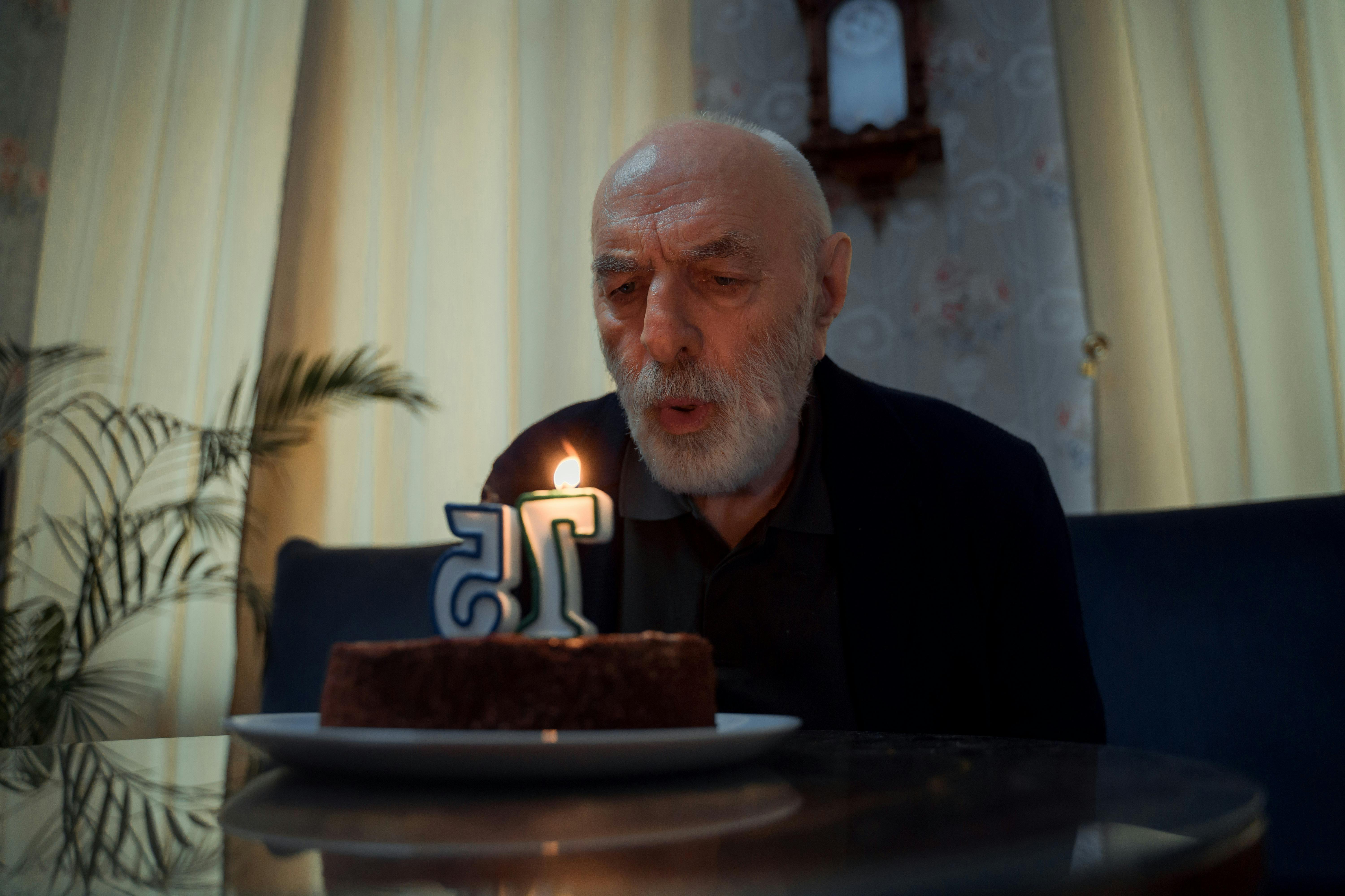 elderly man blowing at his birthday cake