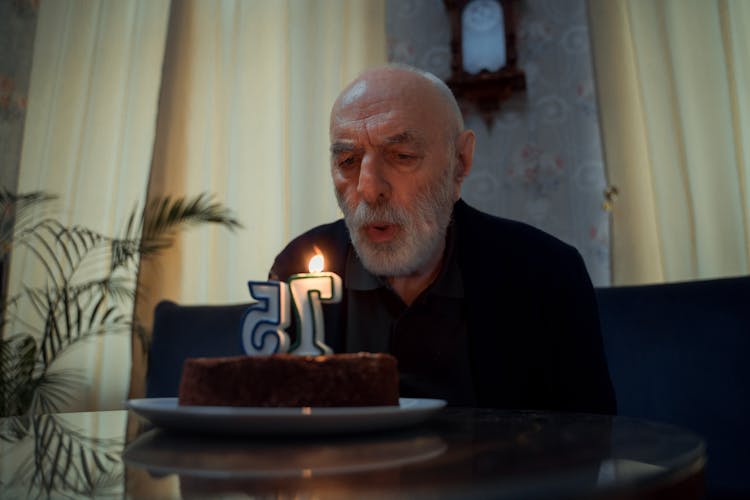 Elderly Man Blowing At His Birthday Cake