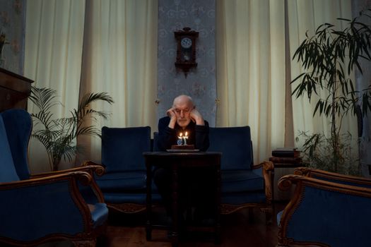 Senior man alone with a birthday cake in a vintage living room setting.