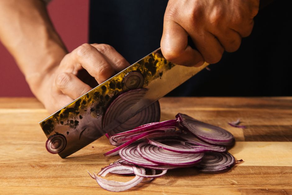 Close-up of chef slicing red onions on a wooden board, showcasing knife skills.