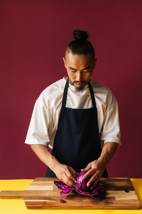 Free Adult male chef in black apron preparing red cabbage on wooden cutting board indoors. Stock Photo