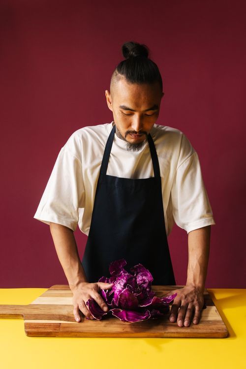 Free Asian chef preparing red cabbage on a wooden board in a modern kitchen setting. Stock Photo