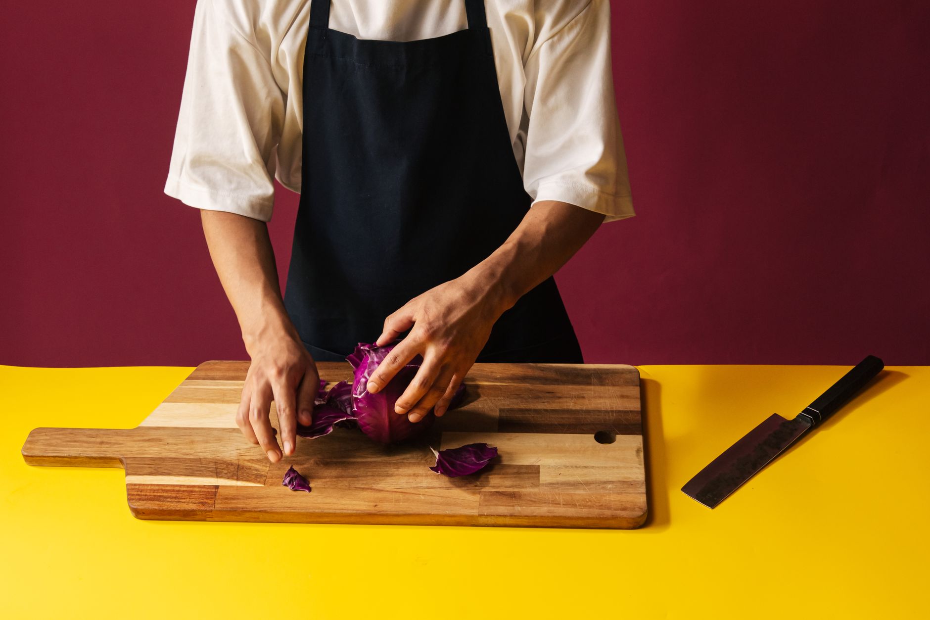 Chef peeling red cabbage on a cutting board with a knife nearby, illustrating culinary skills.
