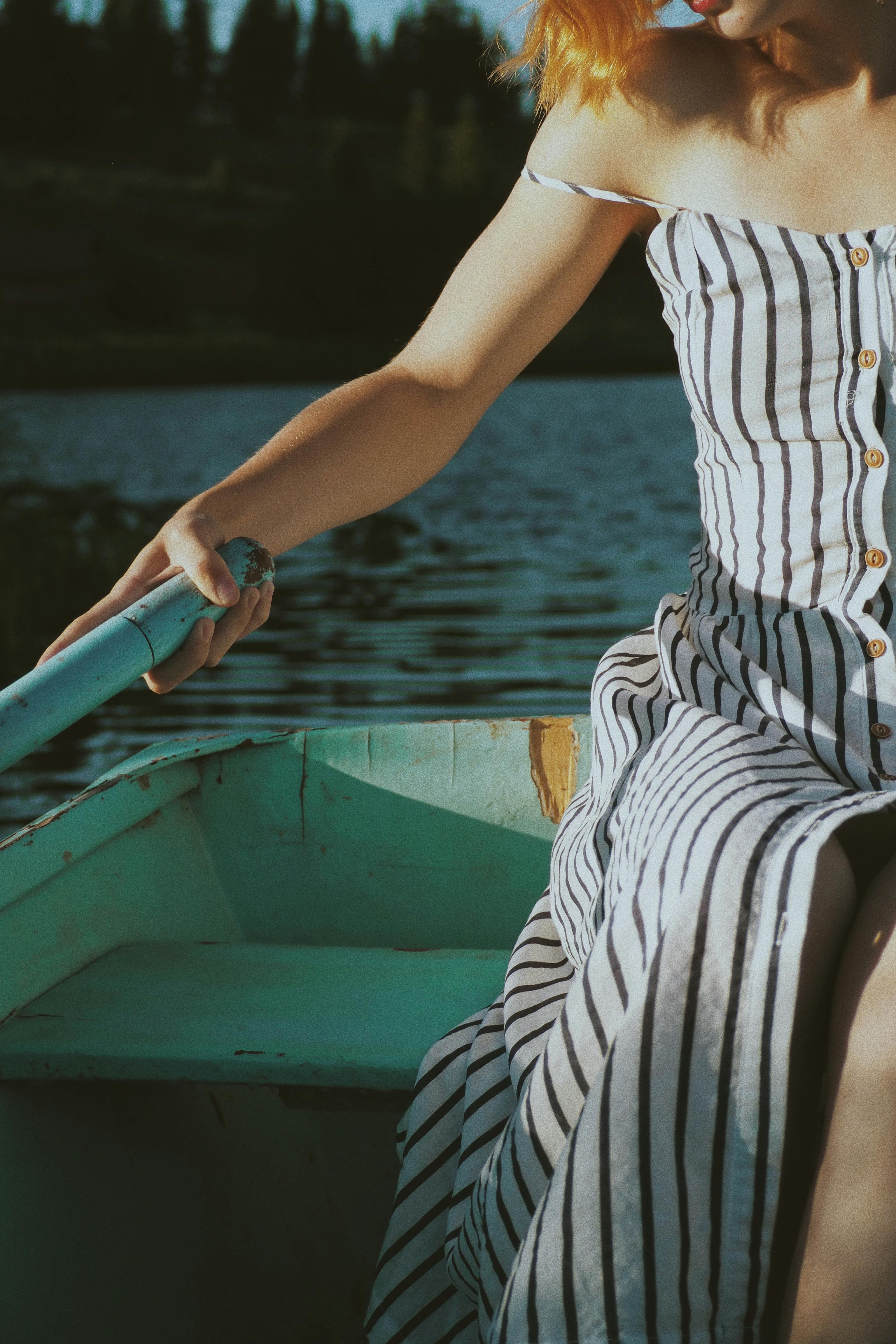 Woman in White and Black Stripe Dress Sitting on Blue Boat