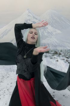 A person in gothic attire posing dramatically in a snowy mountain setting.