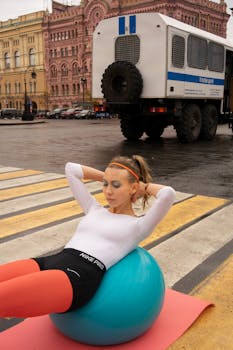 Woman exercising on yoga ball at city crosswalk with historic architecture in the background.