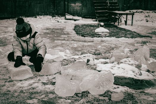 A child interacts with icy blocks outdoors during winter, capturing playful curiosity.