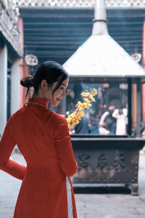 Free Back View of a Woman in a Red Dress Holding Flowers Stock Photo