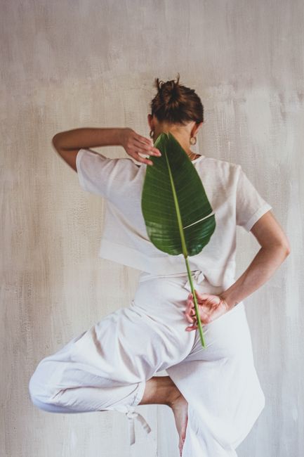 Back view of woman practicing yoga pose holding a banana leaf indoors, promoting wellness and nature.