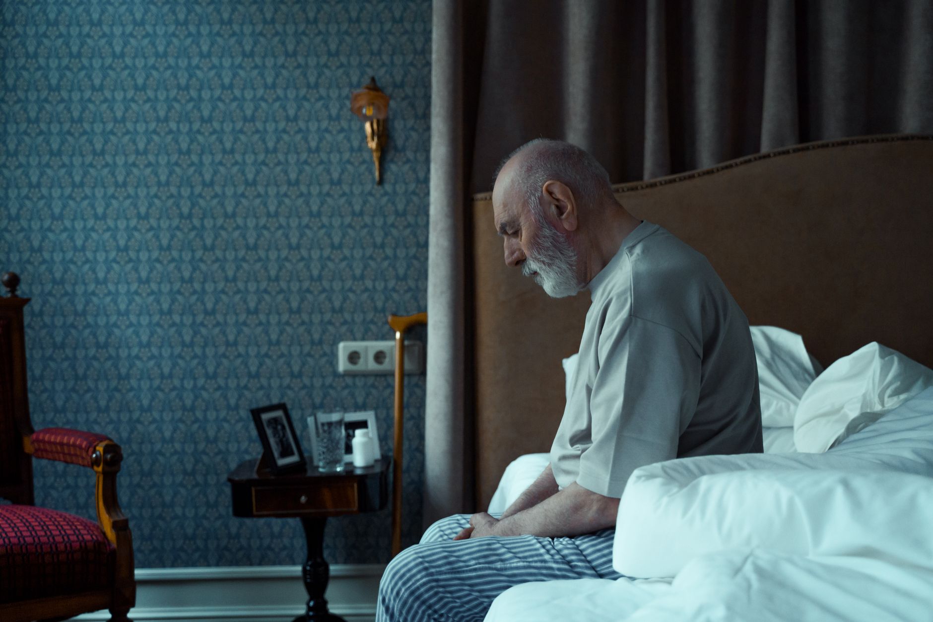Elderly parent sitting alone in dimly lit kitchen looking confused and withdrawn