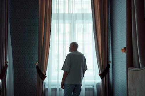 Old Man Standing by the Window Looking Outside