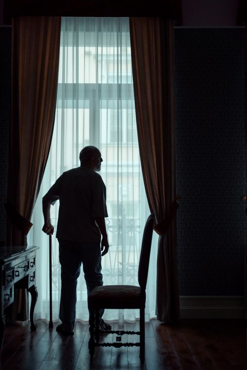 Free Silhouette of a senior adult standing by a window in a dimly lit room. Stock Photo