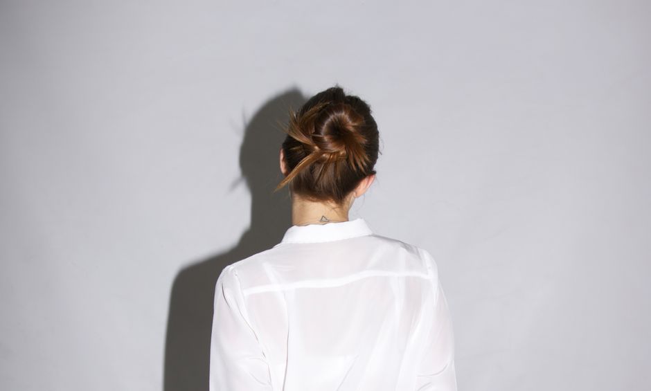 Studio shot of a woman in a white shirt with a hair bun casting a shadow.