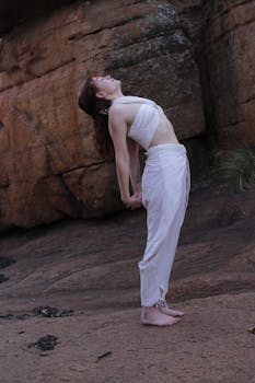 Woman in white attire performing a yoga pose against a rocky backdrop in South Africa.