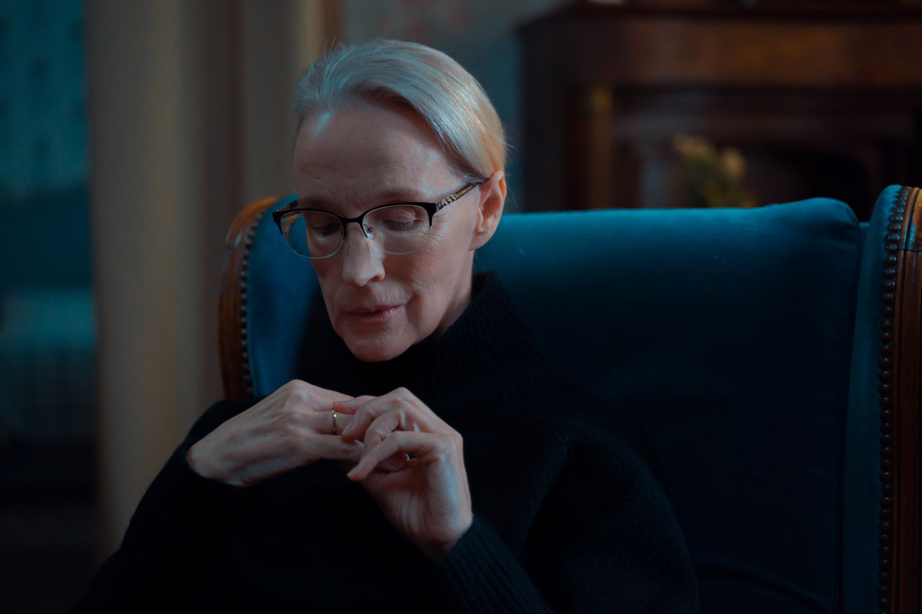 A senior woman with glasses deep in thought indoors, displaying quiet introspection.