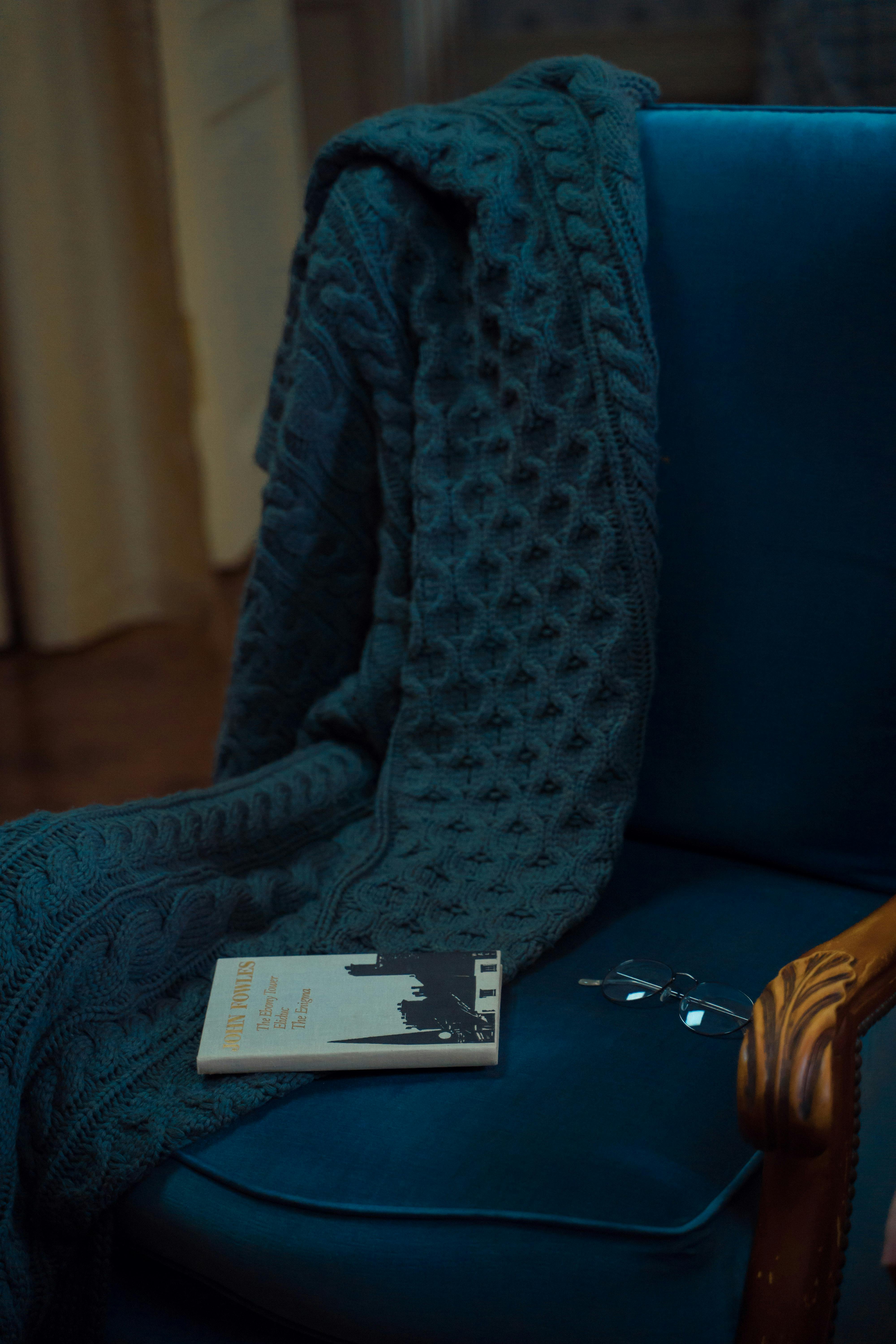A cozy armchair with a knitted blanket, book, and eyeglasses, creating an inviting reading nook.