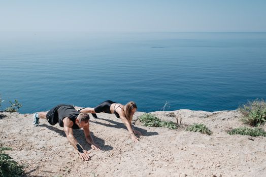 Man and woman performing outdoor exercises on a seaside cliff, promoting fitness and well-being.