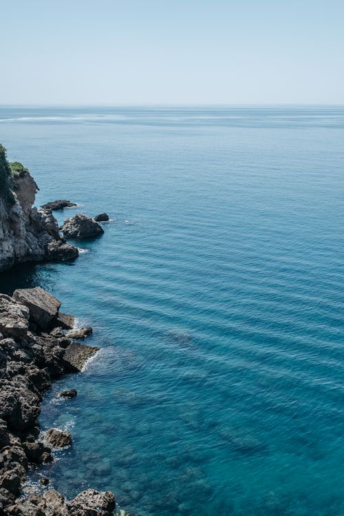 Free Scenic view of a rocky coastal cliff with clear blue ocean under the bright sky. Stock Photo