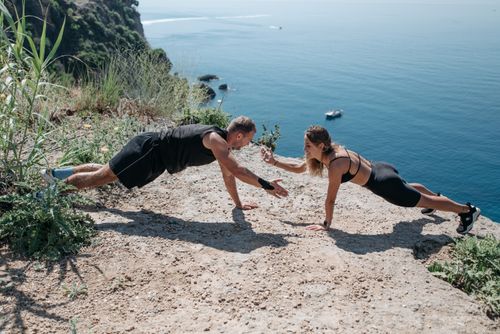 Free A couple performs a workout on a cliff overlooking the sea, embracing outdoor fitness and healthy living. Stock Photo