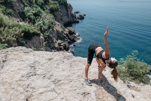 Free A woman in activewear stretches on a cliff overlooking the sea, embracing a healthy lifestyle. Stock Photo
