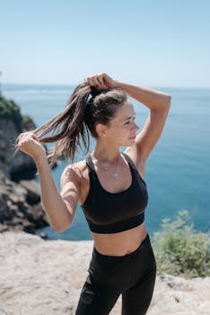 Fit woman in sportswear fixing hair on a cliffside overlooking the ocean.