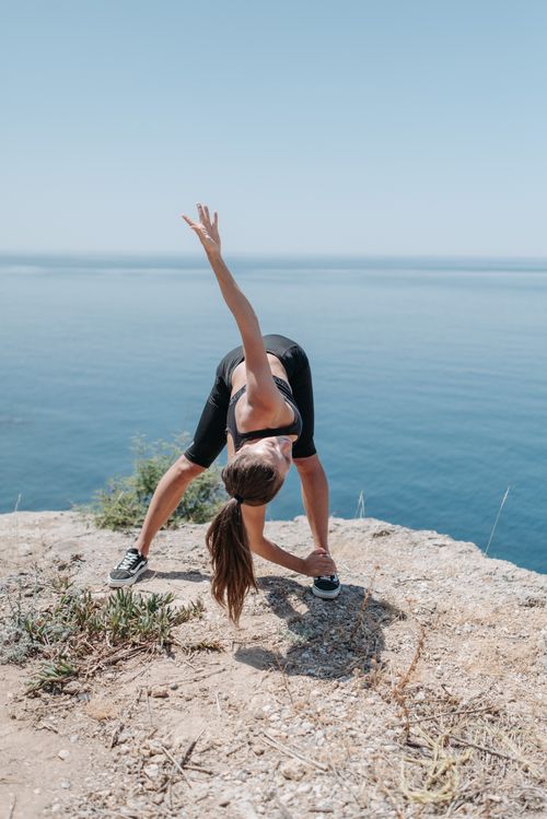 Free A woman performs a stretch on a cliff with a scenic ocean view, embracing fitness and nature. Stock Photo