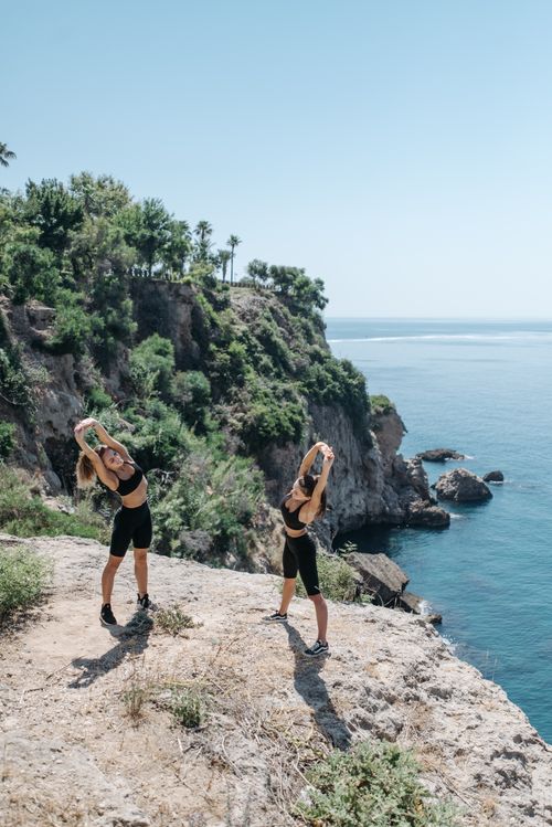 Free Two women stretch on a cliff overlooking the ocean, embracing healthy outdoor fitness. Stock Photo