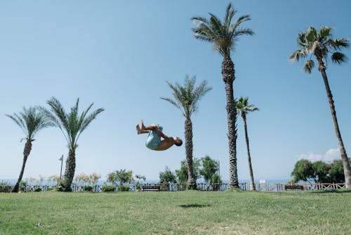 Shirtless Man Doing a Back Flip on Green Grass Field