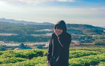 一个穿着黑色连帽衫的年轻人，在郁郁葱葱、阳光明媚、山峦连绵的农田里欢声笑语