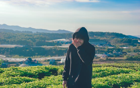 一个穿着黑色连帽衫的年轻人，在郁郁葱葱、阳光明媚、山峦连绵的农田里欢声笑语