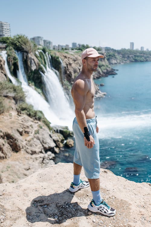 Topless Man in Light Blue Shorts Standing on Rock Formation