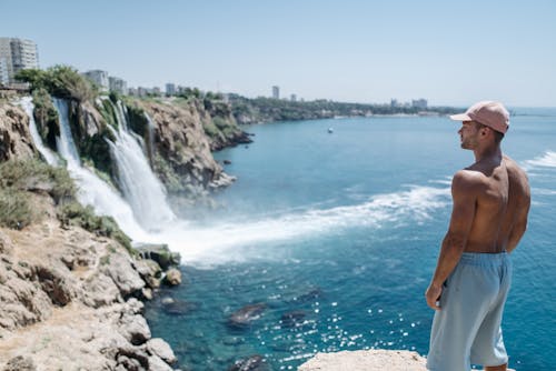 Topless Man Standing on Rocky Shore