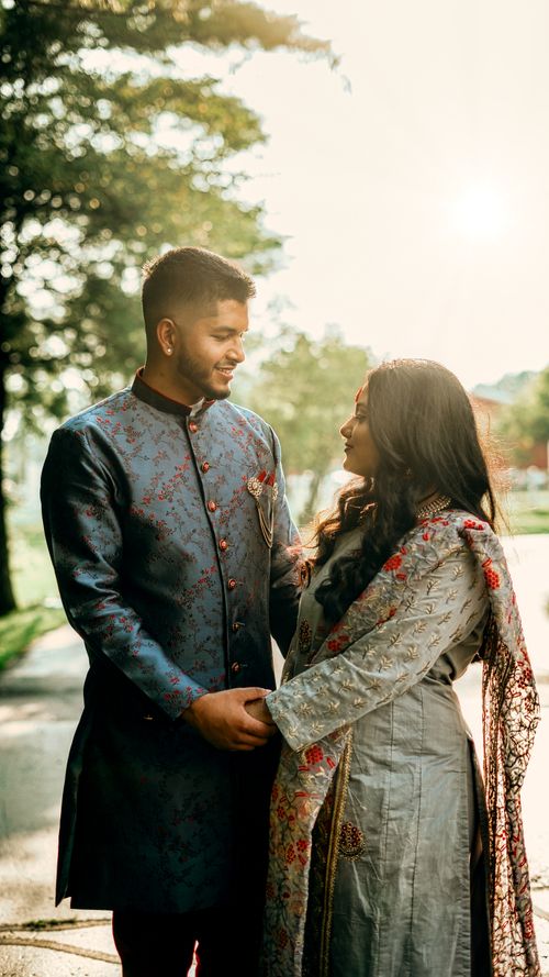 Free Side view of romantic Indian couple wearing traditional outfits holding hands while standing on street with trees during wedding celebration Stock Photo