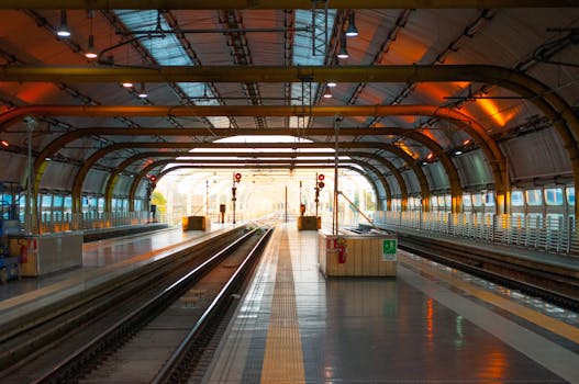 Contemporary railway station featuring a well-lit empty platform and tracks under a steel arch structure.