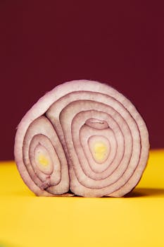 Vibrant sliced red onion on a yellow and burgundy background, showcasing fresh, organic patterns.