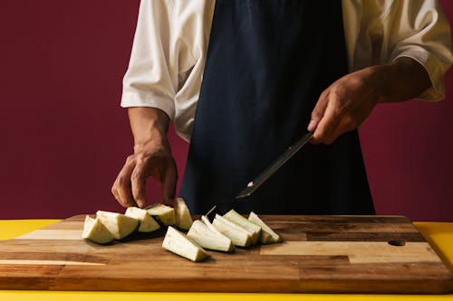 Free Person Slicing Eggplants on a Wooden Chopping Board Stock Photo