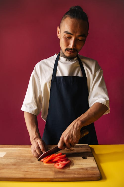 Premium Photo  Man cuts of fresh piece of meat on a wooden cutting board  in the home kitchen. a man in a striped apron with a big knife in his hands
