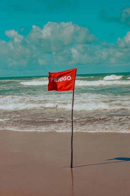 Photo by Leoohigh Red warning flag indicating danger at a tropical beach shore with waves.