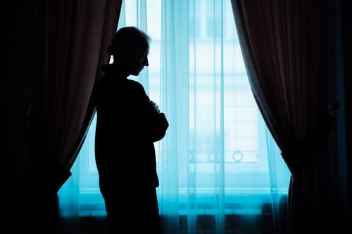 Free A silhouette of a senior woman stands thoughtfully by a window, conveying solitude. Stock Photo
