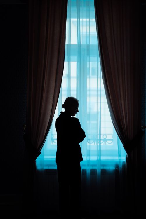Free A woman stands silhouetted against a window with flowing curtains creating a dramatic scene. Stock Photo