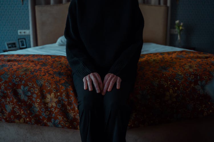 A Person In Black Outfit Sitting On The Edge Of The Bed