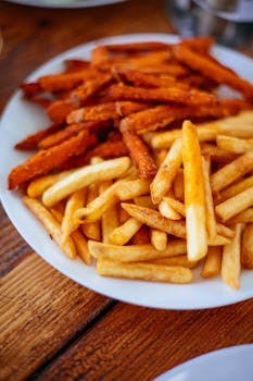 Close-up of delicious French and sweet potato fries on a plate. Perfect for fast food lovers.