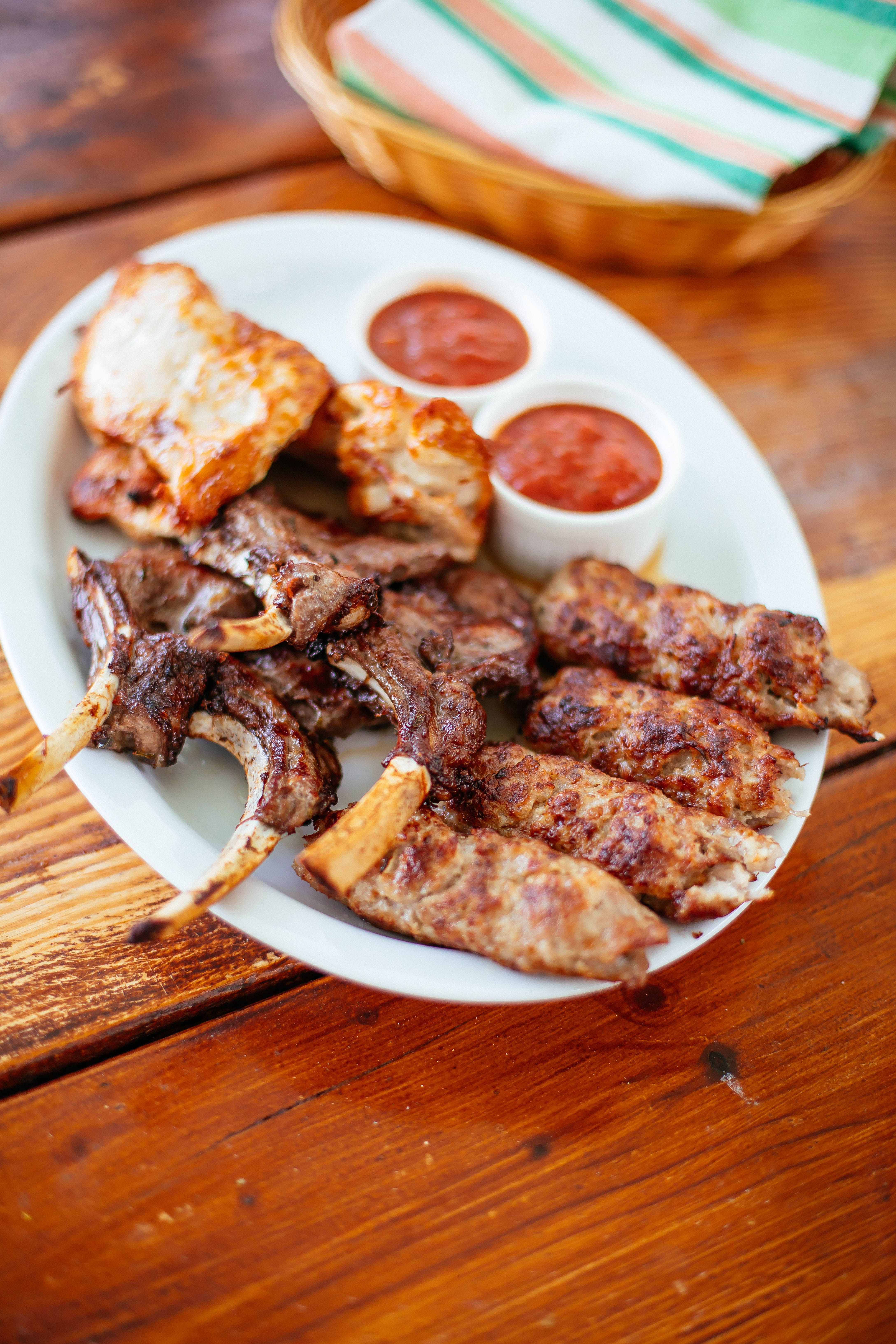 Delicious grilled meat platter with sauces served on a rustic wooden table, perfect for a barbecue feast.