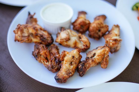 Charred grilled chicken wings and drumettes on white plate with small cup of ranch dip