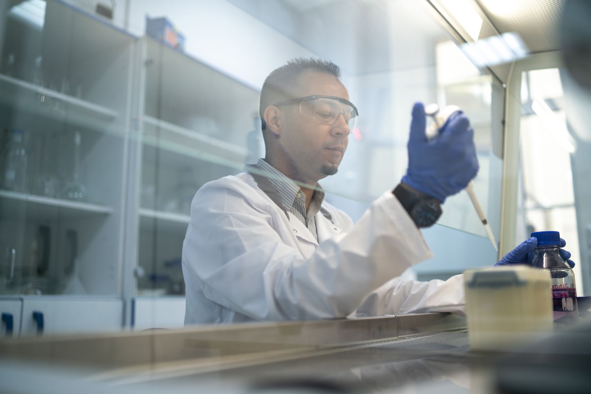 A scientist wearing safety glasses and lab coat conducting research with a pipette in a laboratory.