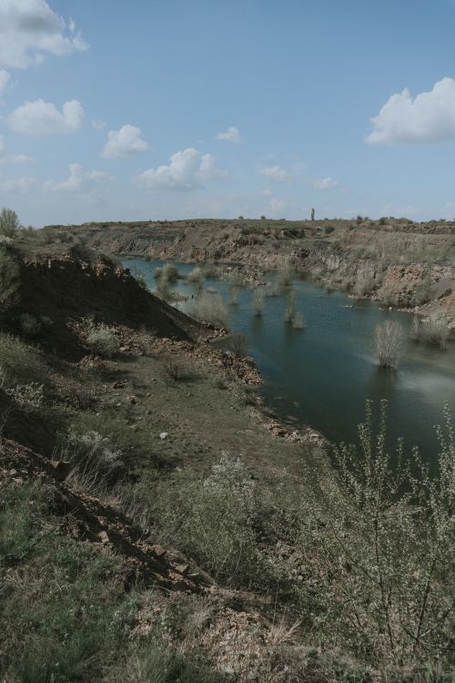 Free Scenic view of a calm river surrounded by rocky terrain and grass under a sunny blue sky. Stock Photo