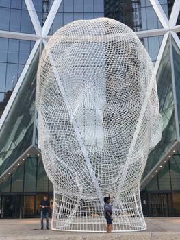 A large modern head sculpture in front of a glass building in Calgary.