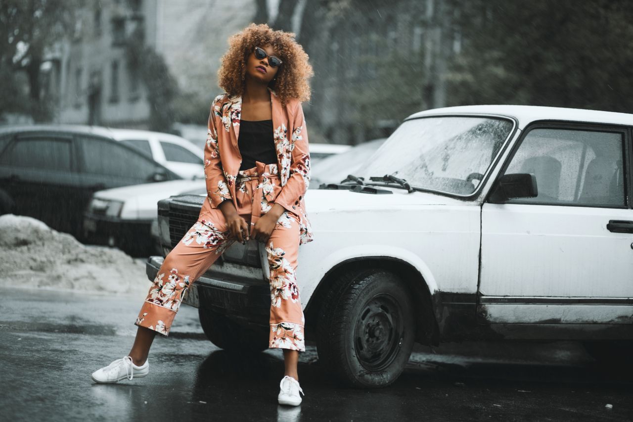 stylish woman in floral suit posing against a classic car on a rainy d